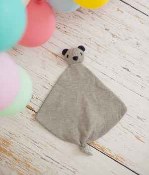 Gray bear-shaped comforter on a wooden floor with colorful balloons in the background