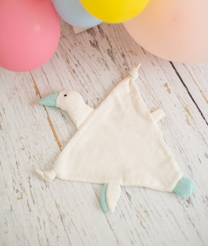 Baby comforter with duck design on a wooden surface with colorful balloons in the background