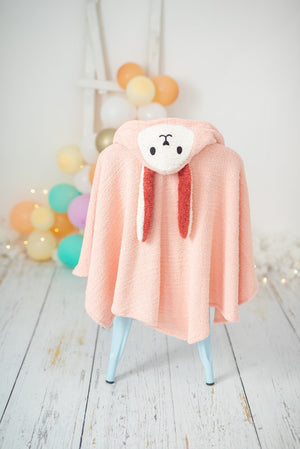 Pink hooded towel with a bear face design on a chair against a light background with colorful balloons.