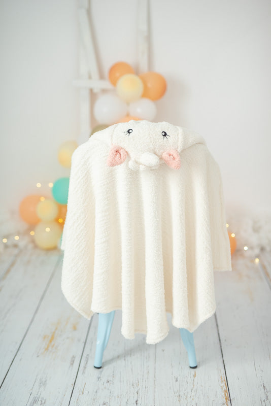 White unicorn hooded towel hanging on a white chair against a light background with colorful balloons.