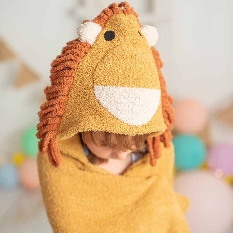 Child wearing a lion-themed hooded towel with colorful balloons in the background