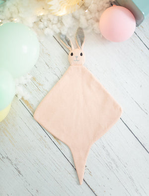 Pink baby comforter with bunny ears on a light wooden surface.