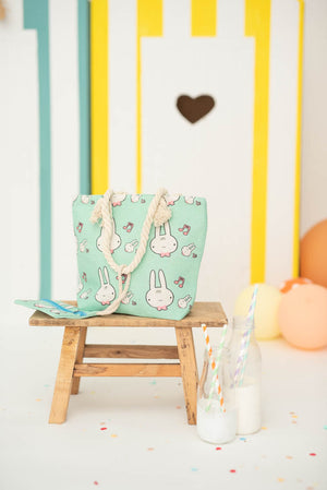 Mint color tote bag with rabbit pattern on a wooden stool against a colorful striped wall.