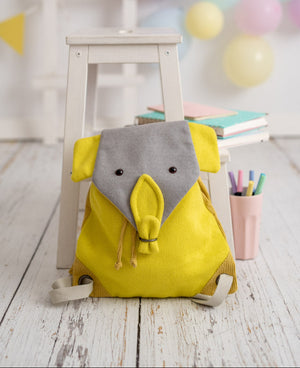 Yellow backpack with elephant design on a wooden floor with balloons in the background