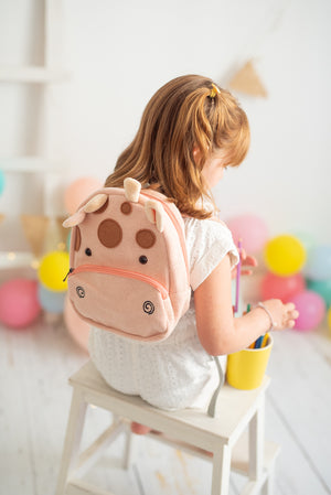 Child sitting on a stool with a cow-themed backpack, colorful balloons in the background