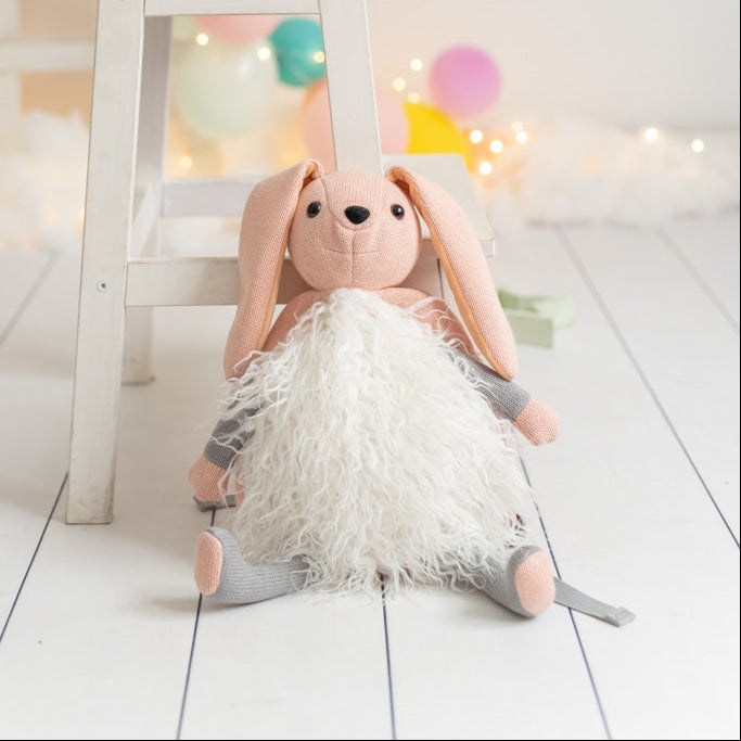 Stuffed rabbit backpack on a white floor with colorful balloons and a small table in the background.
