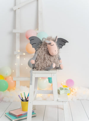 Plush dragon backpack on a white stool with colorful balloons and lights in the background