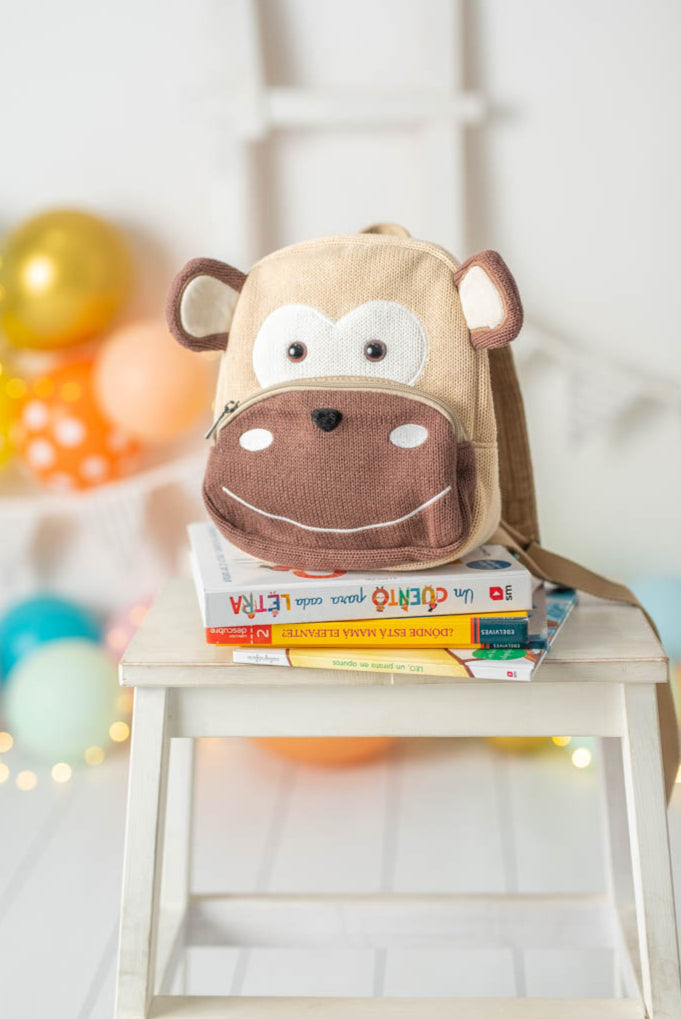 Monkey backpack on a stack of books with colorful balloons in the background