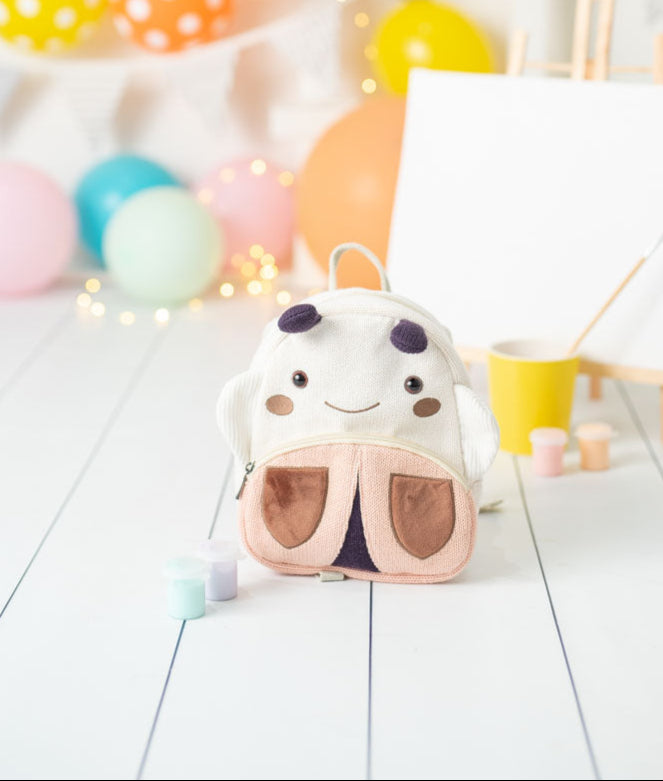 Children's backpack with ladybug design on a white floor with colorful balloons in the background