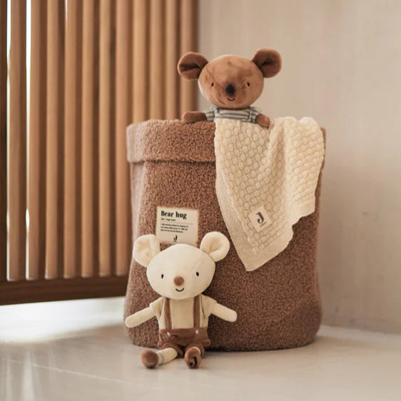 Two teddy bears in a decorative bag against a neutral wall with a wooden panel.