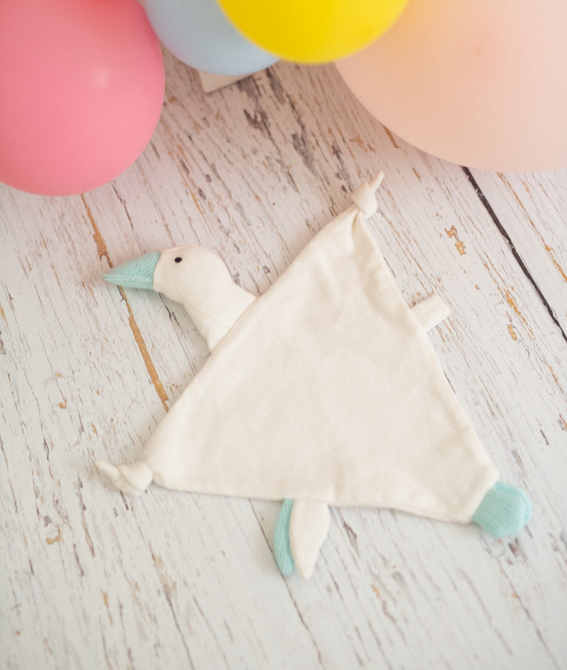 Baby comforter with duck design on a wooden surface with colorful balloons in the background