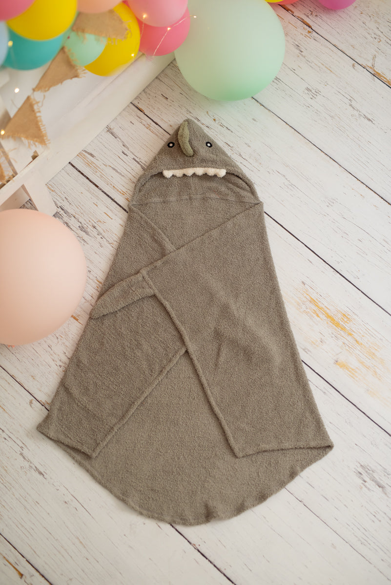 Gray shark-shaped hooded towel on a wooden floor with colorful balloons in the background