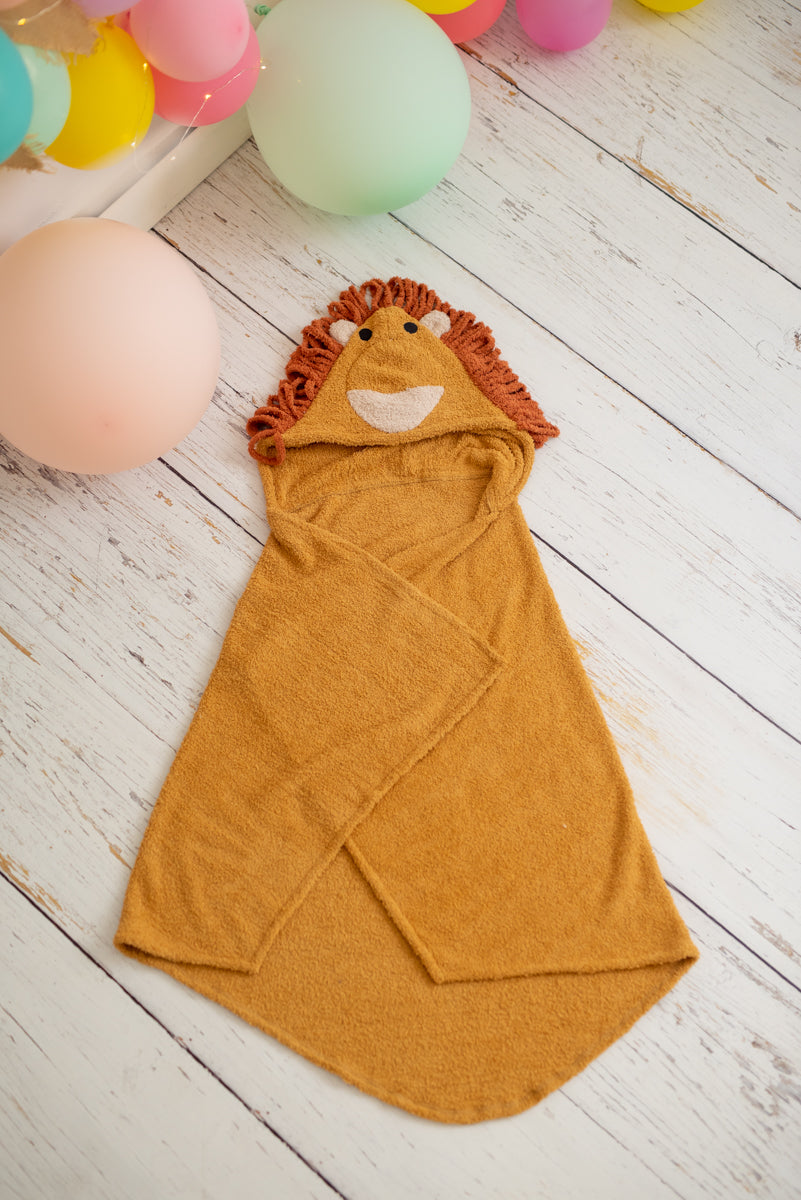 Yellow hooded towel with lion design on a wooden floor with colorful balloons in the background