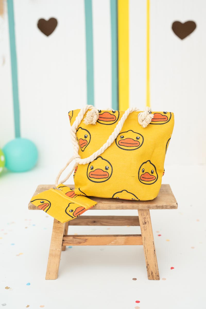 Yellow bag with duck patterns on a small wooden stool against a colorful background